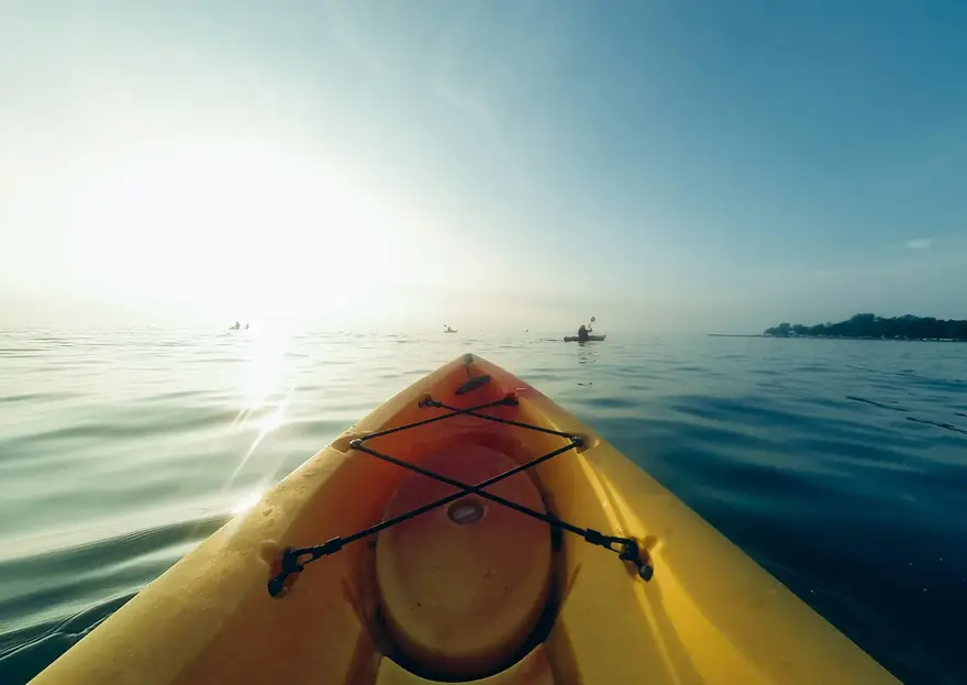 Proa amarela de um caiaque num lago calmo, com o sol baixo